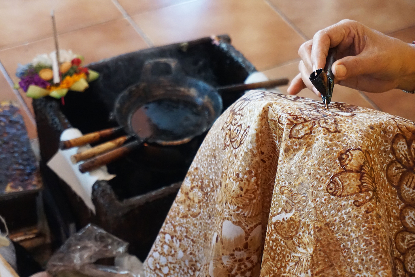 A batik artist dyes hot wax onto cloth using a canting, a traditional tool used in the batik process to draw patterns.